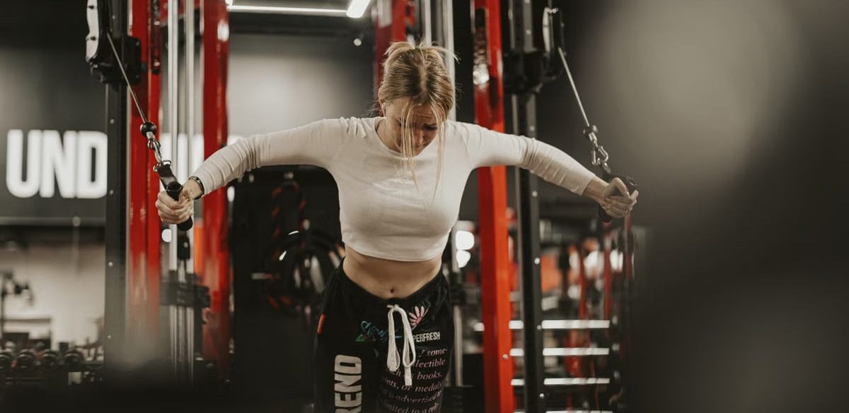 Focused young woman working out using a cable machine in a modern gym environment.